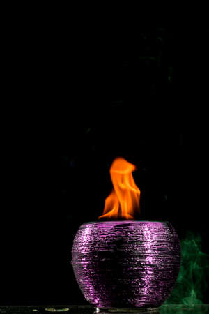 Water mixed with lighter fluid inside a golden pot throwing ice stone to cause thermal shock and cause a splash of liquid with fire on the black background.の写真素材