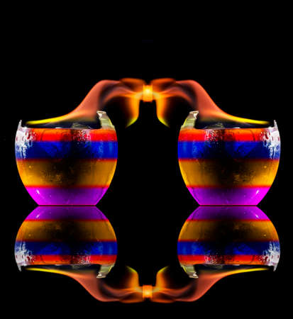 Colored liquid mixed with lighter fluid in a flaming cup where ice cubes are being placed to cause a thermal shock and generate an explosion.の写真素材