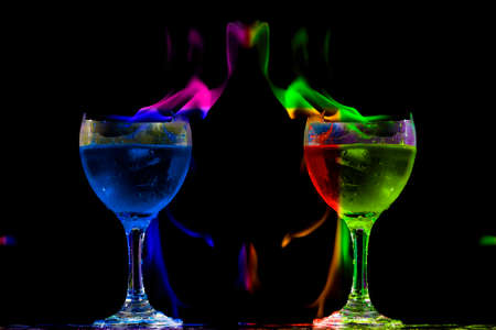 Colored liquid mixed with lighter fluid in a flaming cup where ice cubes are being placed to cause a thermal shock and generate an explosion.の写真素材