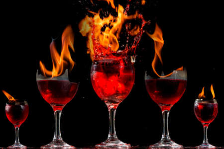 Colored liquid mixed with lighter fluid in a flaming cup where ice cubes are being placed to cause a thermal shock and generate an explosion.の写真素材