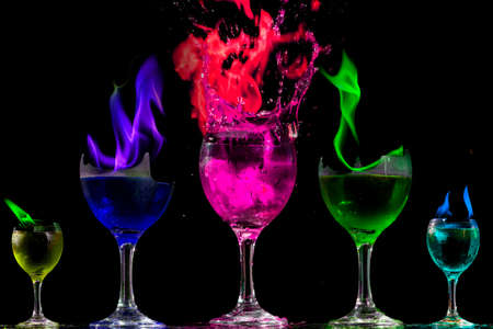 Colored liquid mixed with lighter fluid in a flaming cup where ice cubes are being placed to cause a thermal shock and generate an explosion.の写真素材