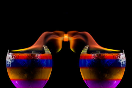 Colored liquid mixed with lighter fluid in a flaming cup where ice cubes are being placed to cause a thermal shock and generate an explosion.の写真素材
