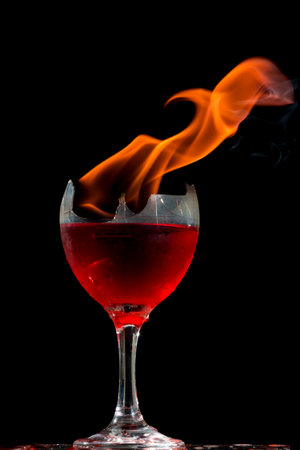 Colored liquid mixed with lighter fluid in a flaming cup where ice cubes are being placed to cause a thermal shock and generate an explosion.の写真素材