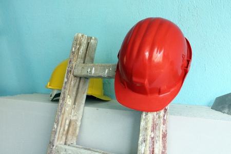 Red helmet and wooden step ladder on work place 