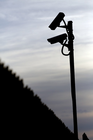 silhouette of two surveillance cameras and a fenceの写真素材