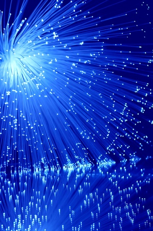 Vibrant blue illuminated fibre optic light strands against blue background and reflecting into the foreground.の写真素材