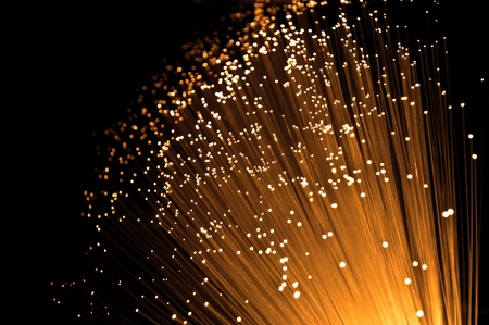 Close up capturing the ends of many golden glowing fibre optic light strands against black.の写真素材