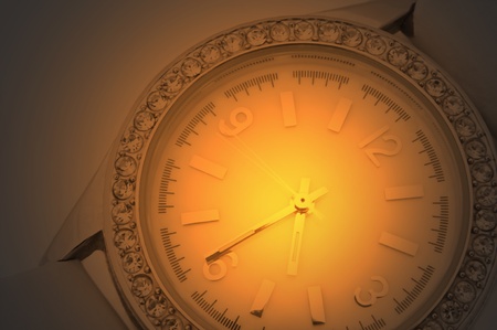 Close up capturing a white and chrome watch face with diamond surround over golden light effect...
