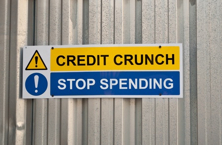 A blue and yellow warning sign with the words CREDIT CRUNCH and STOP SPENDING against metal backgroundの写真素材