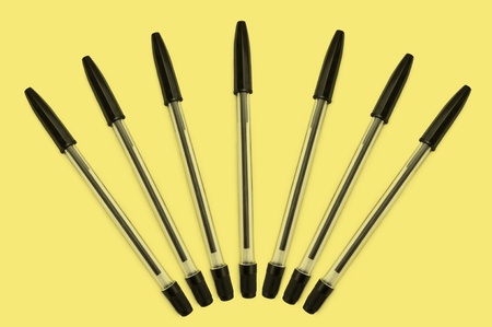 Seven black pens arranged in a fan formation over yellowの写真素材
