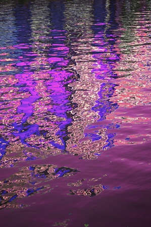 A gently rippled surface on a body of water reflecting blue, pink and red coloursの写真素材
