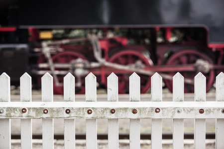 Detail of a fence at a nostalgic railway station with steam locomotive wheels at the background