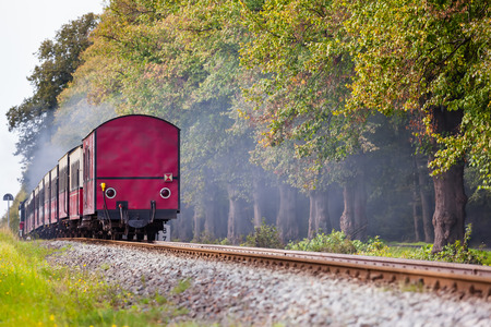 Back of a steam train with a red rail car at the end on a track through beautiful landscapeの写真素材