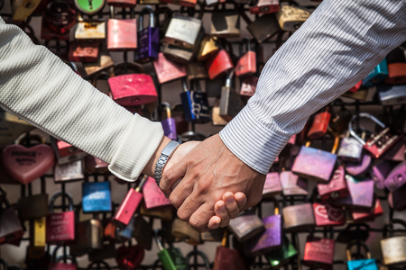 Couple holding hands in front of a background of colorful love locksの写真素材