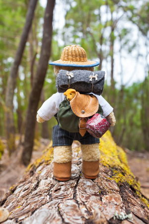 Cute little teddy bear backpacker travels with vintage miniature equipment along tree trunk through forestの写真素材