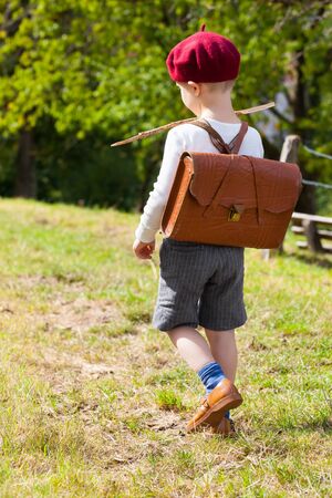 Cute little elementary schoolboy seen from back walk outdoor way to school in nostalgic clothes and satchel (copy space)の写真素材