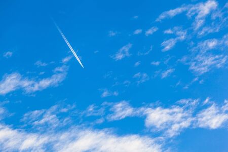 Airplane contrail high up at blue sky at flight between clouds (copy space)の写真素材