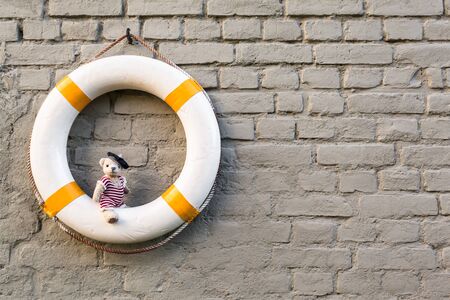 Vintage life buoy at brick wall background and cute little teddy bear wear nostalgic sailor swimsuit sit on it (copy space)の写真素材