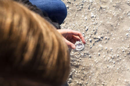 Unrecognizable young woman with group of shells in her hand, sorted by size, at sand beach...