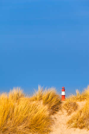 Far red and white lighthouse at dune horizon under blue sky (copy space)の写真素材