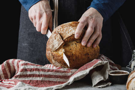Male hands slicing homemade bread with flax on linen towel.の写真素材