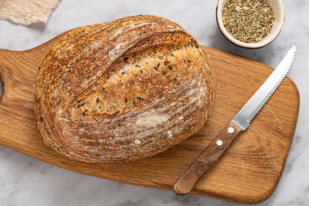 Round loaf of freshly baked sourdough bread with knife on cutting board, top view.