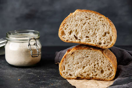 Sliced bread with jar of flour on a black background, two halves of wheat bread. Traditional wheat freshly rustic baked bread.の写真素材