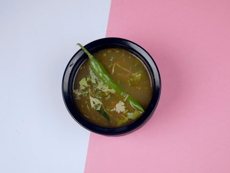 Indian curry in black bowl on pink and white background.