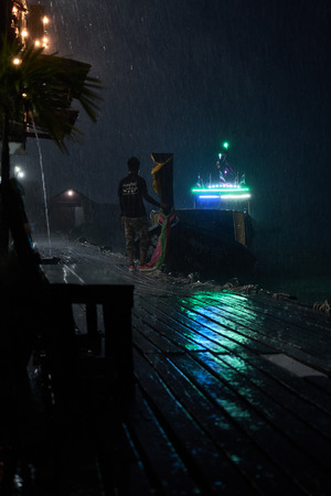 Tropical night rain in Thailand. The guy is meeting boats with guests of seafood restaurantsの写真素材