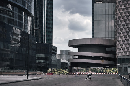 Moscow City skyscrapers in summer in cloudy weather after the rain and a girl on a bike looking on these huge buildingsの写真素材
