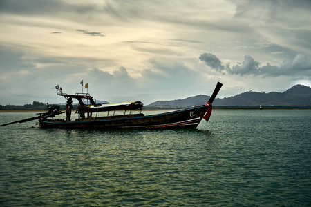 Thai national boat sails on the bay against the background of the cloudy evening skyの写真素材