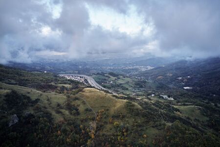 Autumn alpine speed road in Italia. Aerial view from above with clouds on the background and village far awayの写真素材