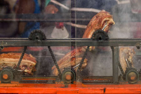 Large cuts of pork belly being roasted over hot charcoals and being turned evenly by use of a motor, cogs and a chain in the Philippines.の写真素材
