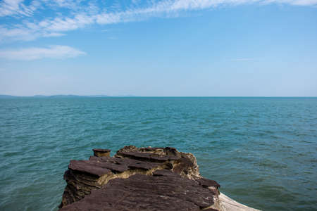 Rock island in foreground of a calm sea and a clear sky with land in the far distance.の写真素材