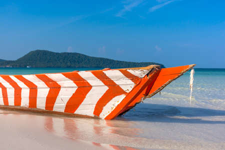 Old Red and White wooden boat left to rot on a white sand beach in a tropical beach bay.
