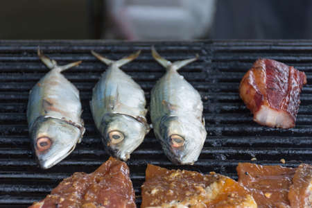 Fish cooking on a BBQ grill with other meats.の写真素材