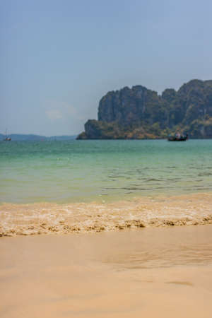 Light waves run up a sandy Thai beach with rocky island back drop.の写真素材
