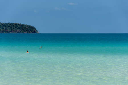 Two people in a crystal clear calm tropical sea with headland on the horizon.の写真素材