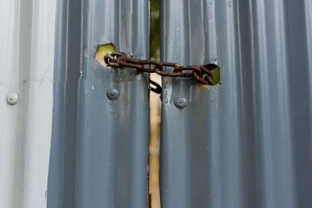 Painted corrugated metal gate padlocked shut with a rusty heavy duty metal chain.