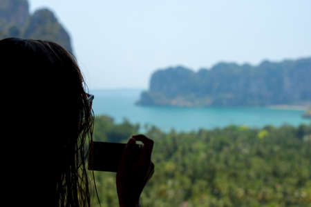 A Young woman taking a photo from a high viewpoint over looking Railay Beach, South Thailand.の写真素材