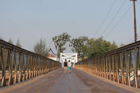 the backs of two children walking away across a metal river crossing bridge in Cambodia.の写真素材