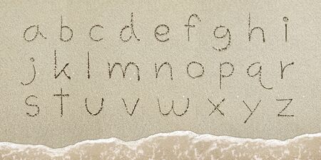 Alphabet letters handwritten in the sand on the beach
