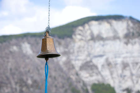 A bell with a blue string on a blurry background in the mountains.の写真素材