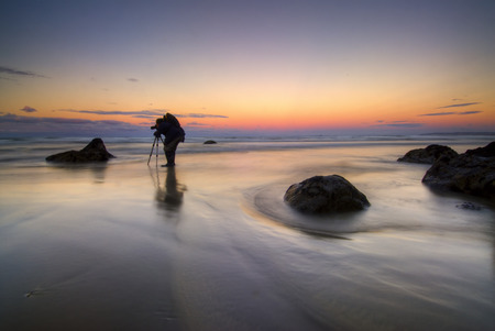 Photographer taking photos on beach at dawn New Zealand