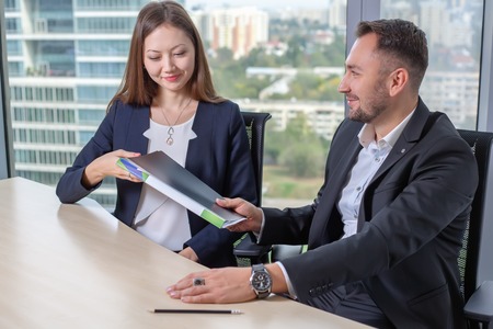 Young asian business woman in suit discusses the report with his colleague at work in office. Man...