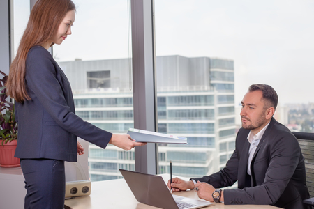 Young Asian business woman in suit brought the report to her bossの写真素材