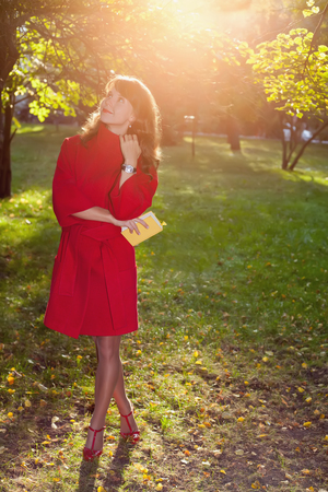 Beautiful woman in red coat posing in autumn Park, keeping in hand little yellow bookの写真素材