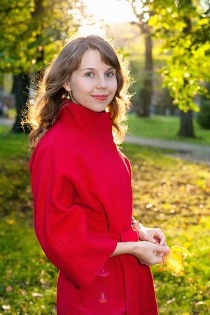 Beautiful woman in red coat posing in autumn Park with a leaves in his handsの写真素材