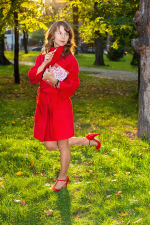 Beautiful woman in red coat posing in autumn Park with a book in his handsの写真素材
