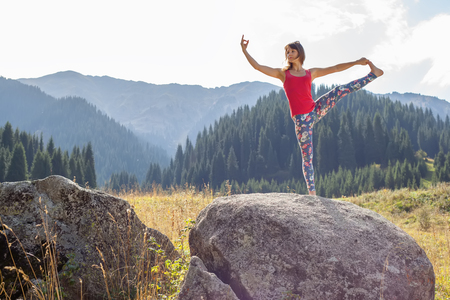 young woman doing yoga on a rock, on a background of mountainsの写真素材